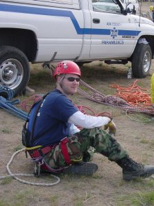 paramedic in climbing gear sitting on the ground next to a truck