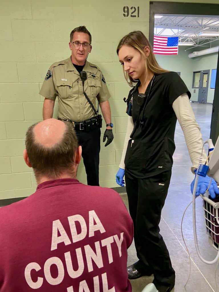 Nurse in Black Scrubs with a sheriff deputy talking to an inmate