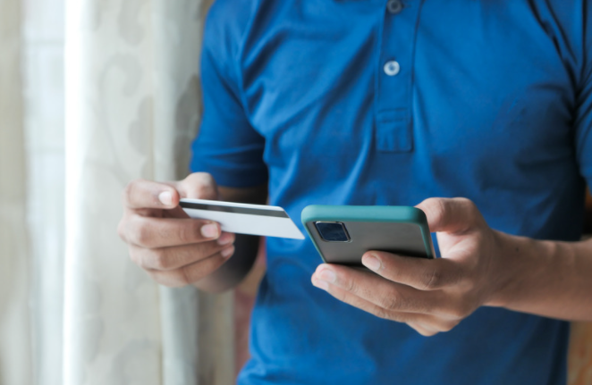 Person in a blue golf shirt holding a phone and debit card